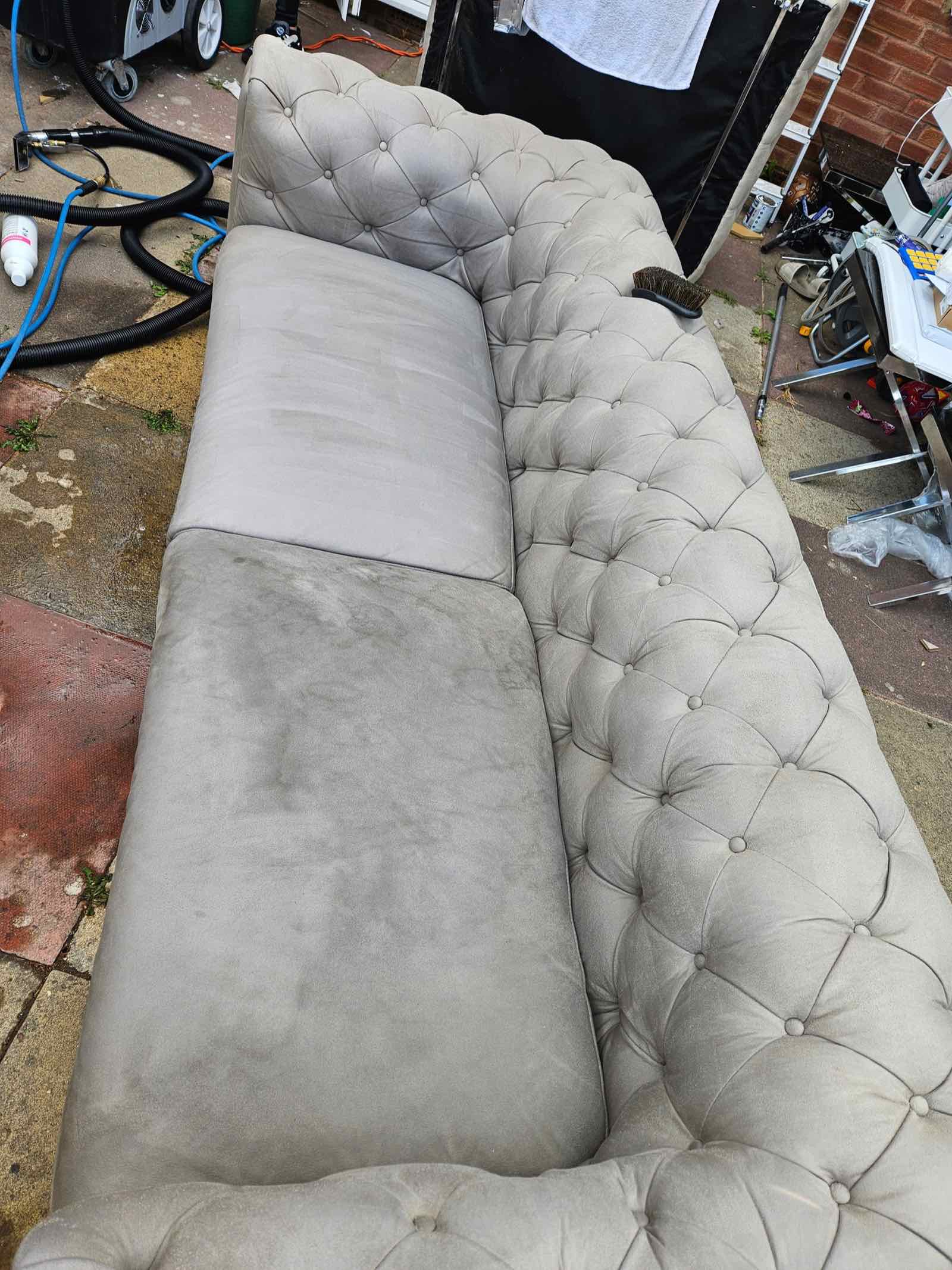 Grey buttoned Chesterfield-style sofa part-way through a steam clean, with visible difference between the cleaned and uncleaned cushion
