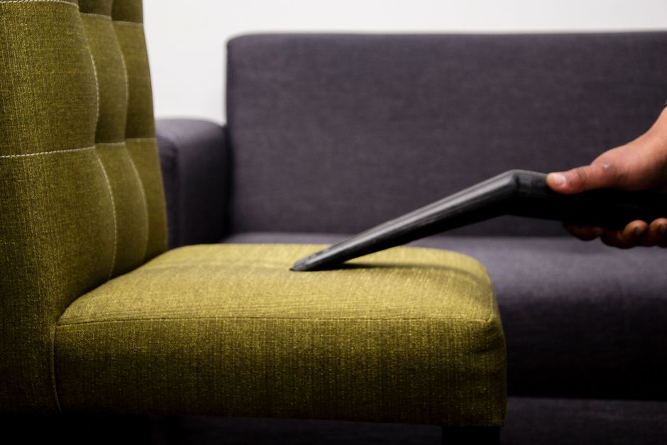 Steam cleaning wand being run across a green fabric armchair cushion